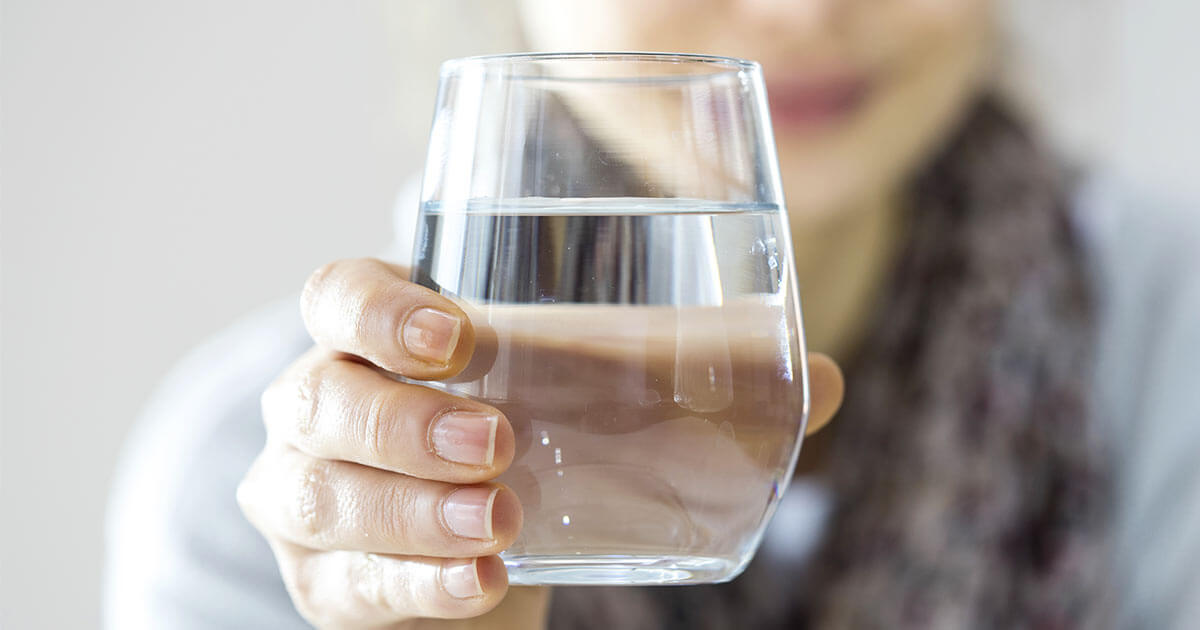 How to Cleanse Heavy Metals from the Body Woman holding out a glass of water